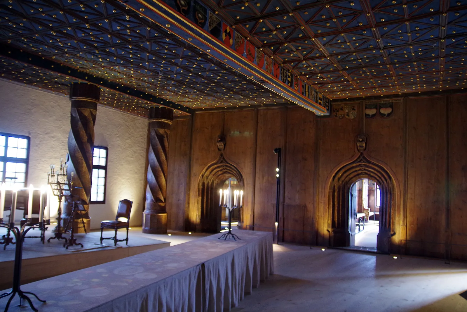 A hall in the fortress's Prince's Chambers with a dark ceiling set with gold stars, twisted wooden pillars, a long table and candlesticks